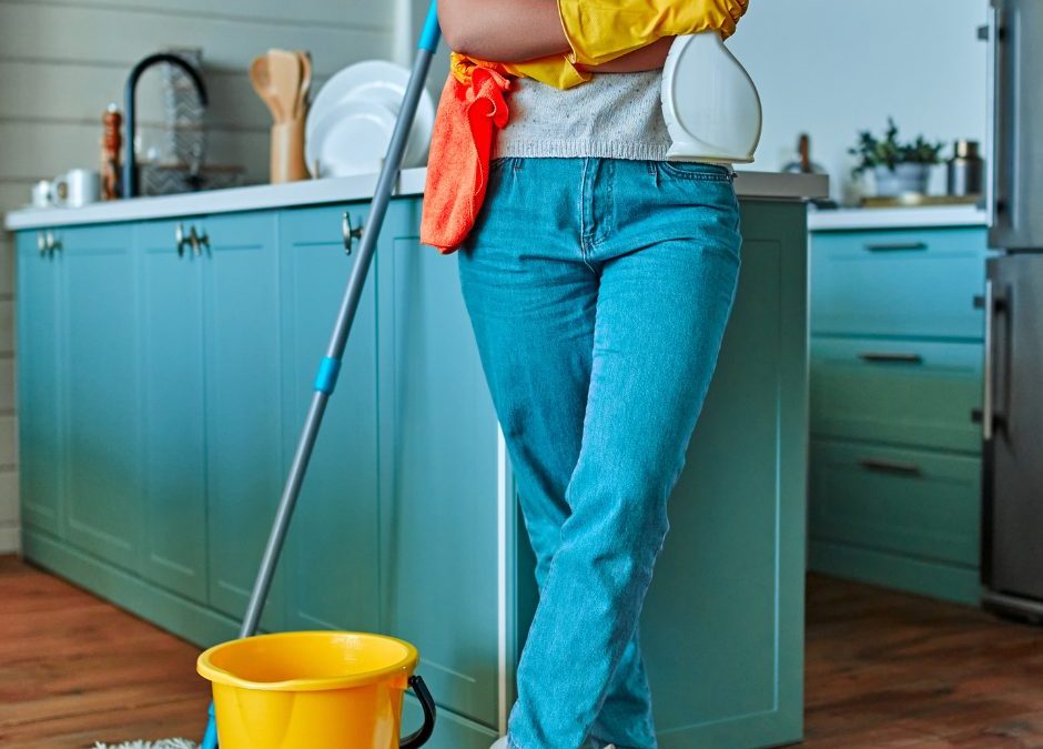 person holding cleaning supplies leaning against kitchen counter
