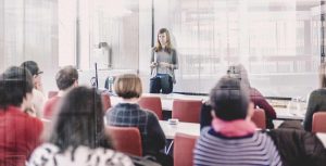woman giving a presentation in front of rows of people at tables